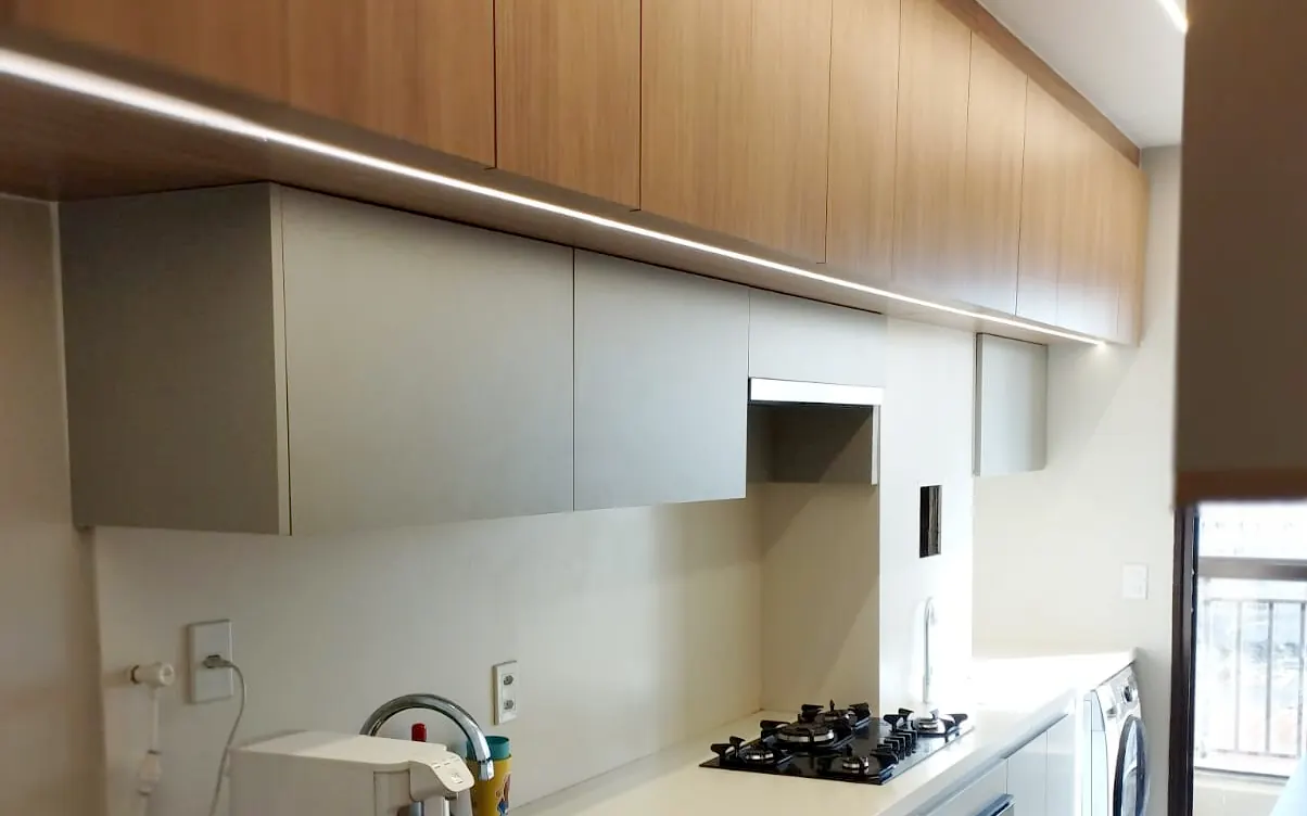 Cozinha planejada em MDF amadeirado com fita de LED embutida sob os aéreos, em apartamento de Brasília DF