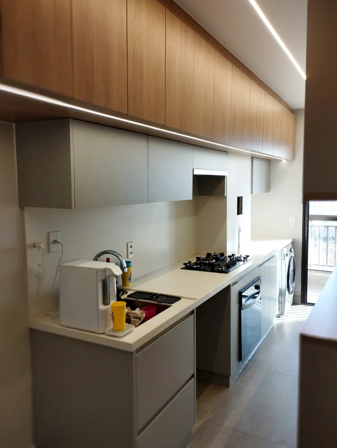 Cozinha planejada em MDF amadeirado e cinza com fita de LED embutida, em apartamento de Brasília